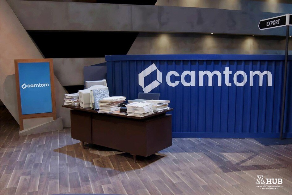 foro de shark tank con escritorio y contendor maritimo con logotipo de camtom