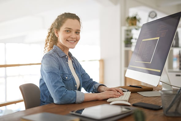 mujer en su escritorio que teclea mientras está sonriendo enfrente de su computadora