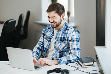 hombre trabaja en una oficina con su computadora mientras sonrie