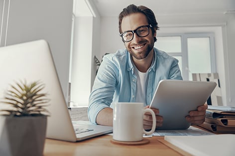 hombre sonriendo con su ipad y computadora en su oficina 