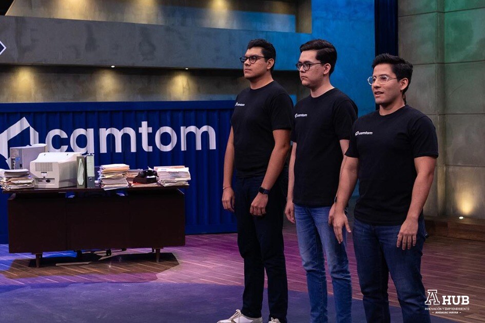 tres personas en el foro de shark tank con un escritorio y un contenedor al fondo