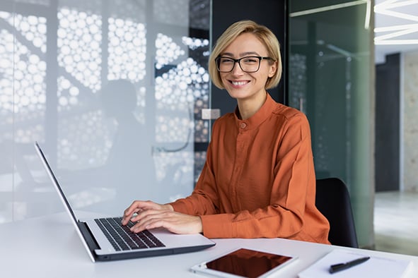 mujer sonrie mientras trabaja con su computadora en una oficina