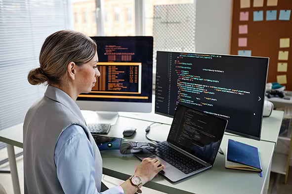 chica que se encuentra programando en su oficina con varias computadoras