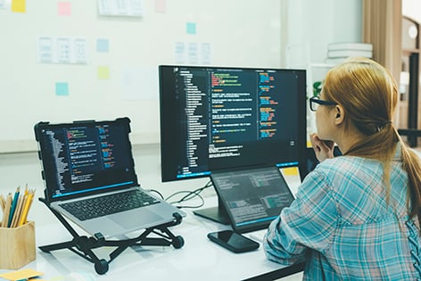 Persona enfrente de dos computadoras que está programando
